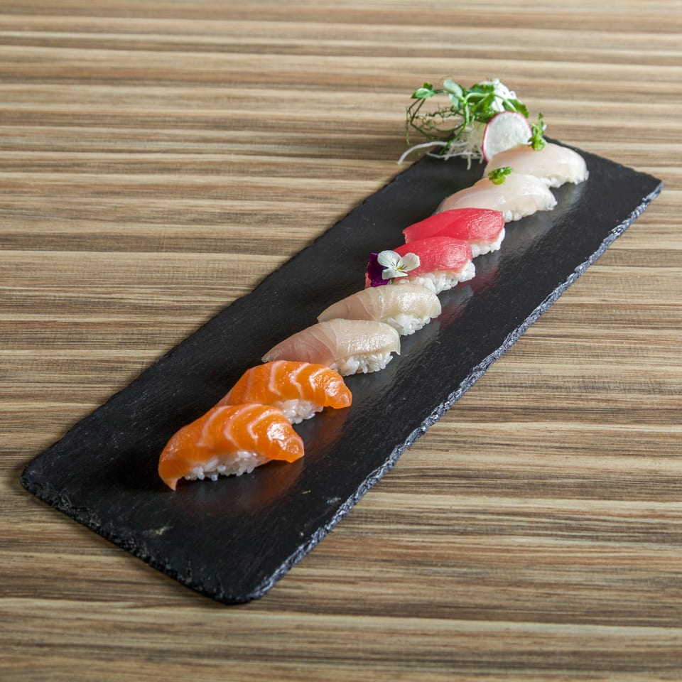 Assorted salmon and tuna nigiri sushi arranged on a black slate platter with radish and greens garnish.