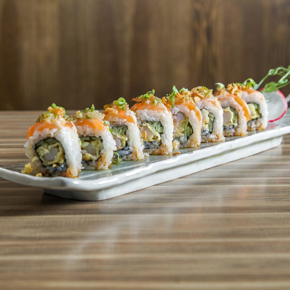 Sushi rolls topped with salmon, crispy onions, and green onions arranged on a rectangular white platter.